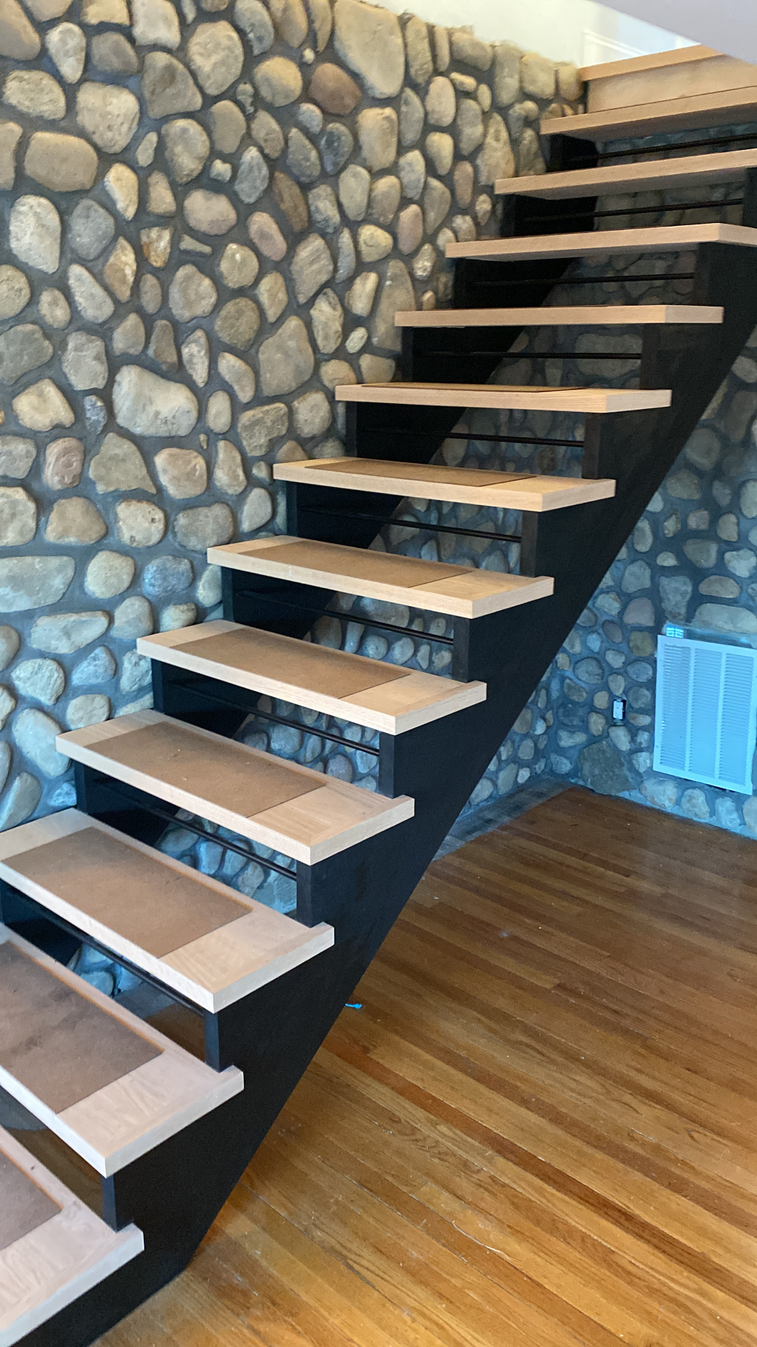 Modern floating staircase with white oak treads against stone wall